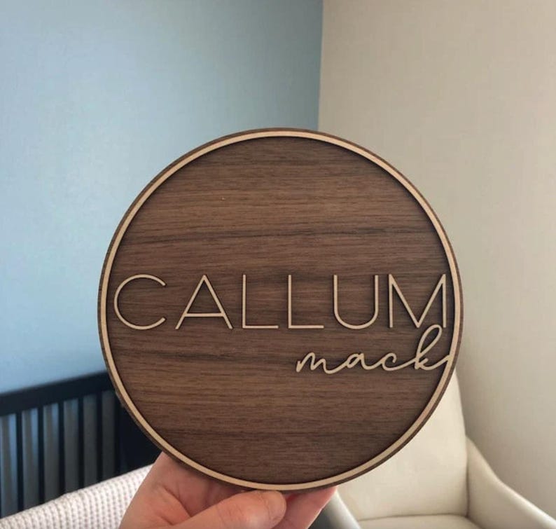 Op de afbeelding: Een rond houten bord met een lichtbruine houtnerf. Het bord heeft een witte rand en de naam "CALLUM mack" is gegraveerd in witte letters.