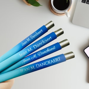May include: Four blue and silver personalized pens with the name "Jean M. Danckaert" engraved on each pen.