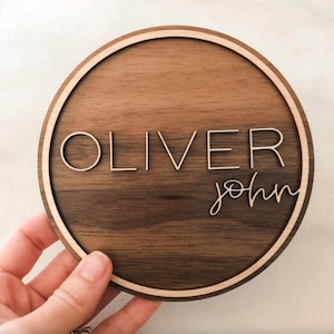 Op de afbeelding: Een rond houten bord met een lichtbruine houtnerf en een lichtbruine rand. Het bord heeft de naam "Oliver John" gegraveerd in wit.