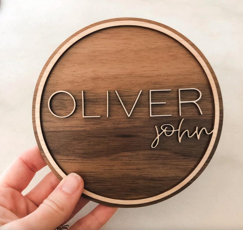 Op de afbeelding: Een rond houten bord met een lichtbruine houtnerf en een lichtbruine rand. Het bord heeft de naam "Oliver John" gegraveerd in wit.