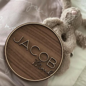 Op de afbeelding: Een rond houten bord met de naam "Jacob Mark" gegraveerd in een modern lettertype. Het bord is gemaakt van donker walnoot hout en heeft een lichtbruine rand.