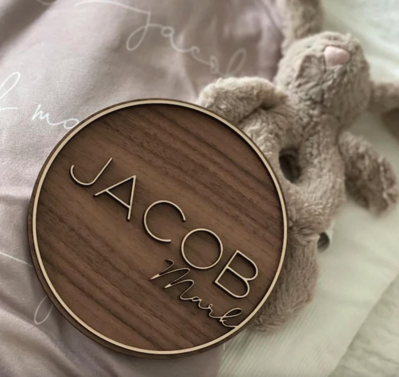 Op de afbeelding: Een rond houten bord met de naam "Jacob Mark" gegraveerd in een modern lettertype. Het bord is gemaakt van donker walnoot hout en heeft een lichtbruine rand.