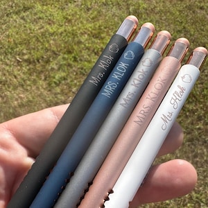 May include: Five personalized stylus pens with rose gold accents. The pens are black, dark blue, gray, rose gold, and white. Each pen has the name "Mrs. Klok" or "Ms. Klok" engraved on it.