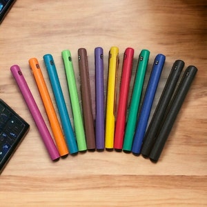 Puede incluir: Un conjunto de 12 fundas para tel&eacute;fono de colores dispuestas en semic&iacute;rculo sobre una superficie de madera. Las fundas est&aacute;n hechas de un material texturizado y est&aacute;n disponibles en una variedad de colores, incluyendo morado, verde, azul, naranja, amarillo y rojo.