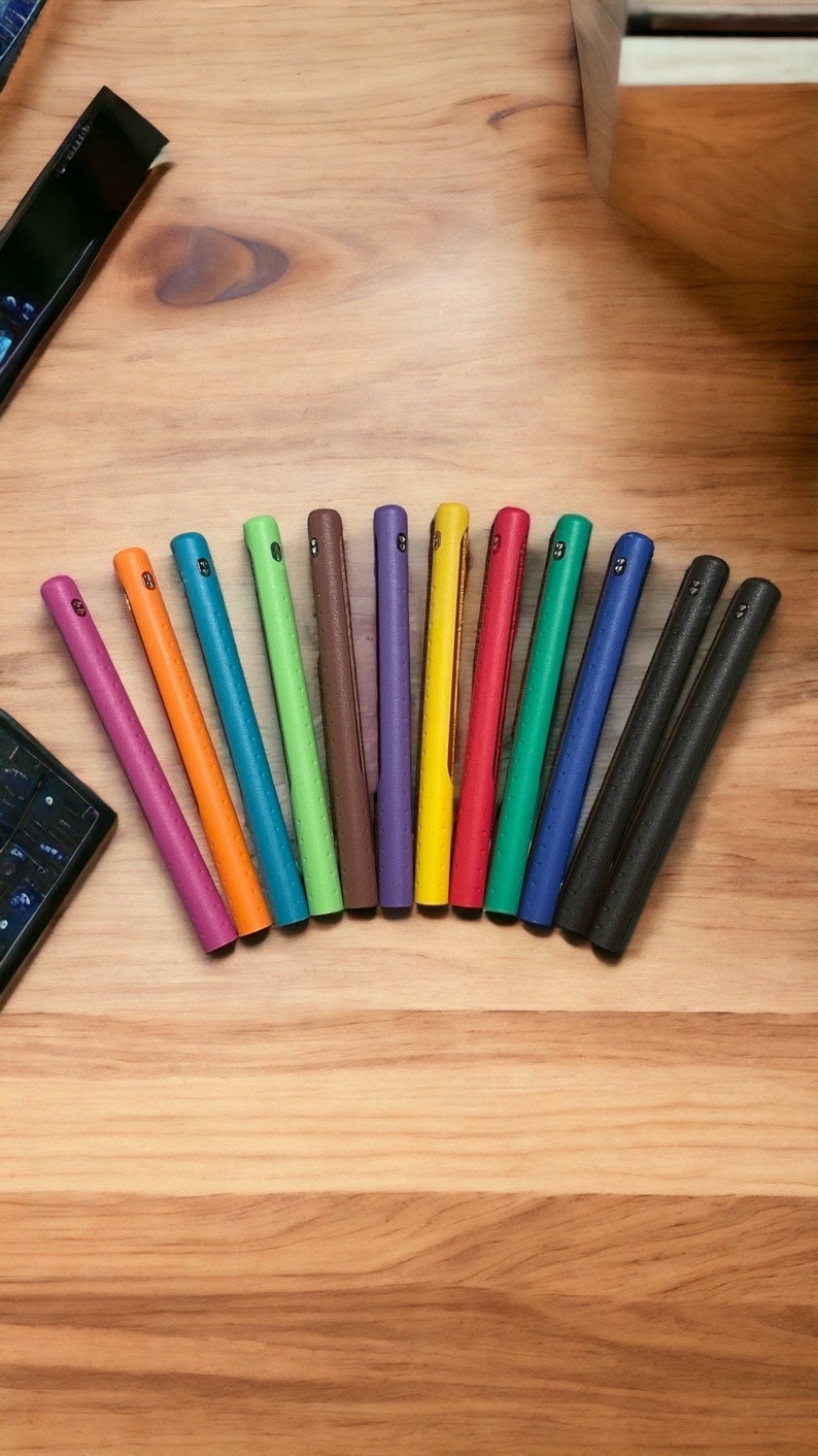 Puede incluir: Un conjunto de 12 fundas para tel&eacute;fono de colores dispuestas en semic&iacute;rculo sobre una superficie de madera. Las fundas est&aacute;n hechas de un material texturizado y est&aacute;n disponibles en una variedad de colores, incluyendo morado, verde, azul, naranja, amarillo y rojo.