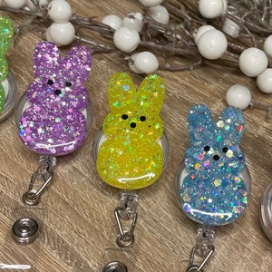 Op de afbeelding: Vijf kleurrijke konijnenvormige sleutelhangers met glitter ingebed in de hars. Elke sleutelhanger is bevestigd aan een intrekbare badgehouder.