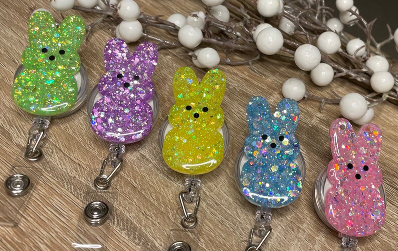 Op de afbeelding: Vijf kleurrijke konijnenvormige sleutelhangers met glitter ingebed in de hars. Elke sleutelhanger is bevestigd aan een intrekbare badgehouder.