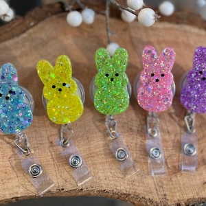 Op de afbeelding: Vijf kleurrijke konijnenvormige sleutelhangers met glitteraccenten. Elke sleutelhanger heeft een andere kleur: blauw, geel, groen, roze en paars.