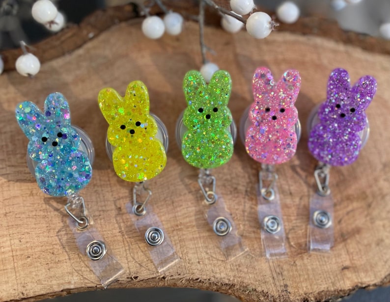 Op de afbeelding: Vijf kleurrijke konijnenvormige sleutelhangers met glitteraccenten. Elke sleutelhanger heeft een andere kleur: blauw, geel, groen, roze en paars.