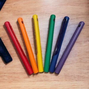 Puede incluir: Siete agarres de palo de golf de colores dispuestos en forma de arco&iacute;ris sobre una superficie de madera. Los agarres son de goma y tienen una superficie texturizada.