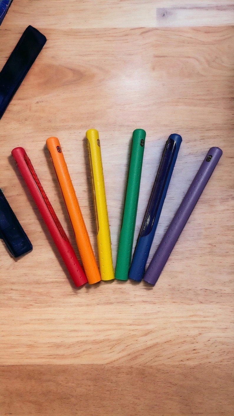Puede incluir: Siete agarres de palo de golf de colores dispuestos en forma de arco&iacute;ris sobre una superficie de madera. Los agarres son de goma y tienen una superficie texturizada.