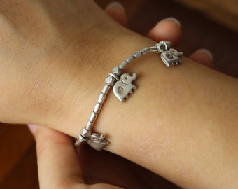 May include: A silver bracelet with multiple elephant charms. The bracelet is on a person's wrist.