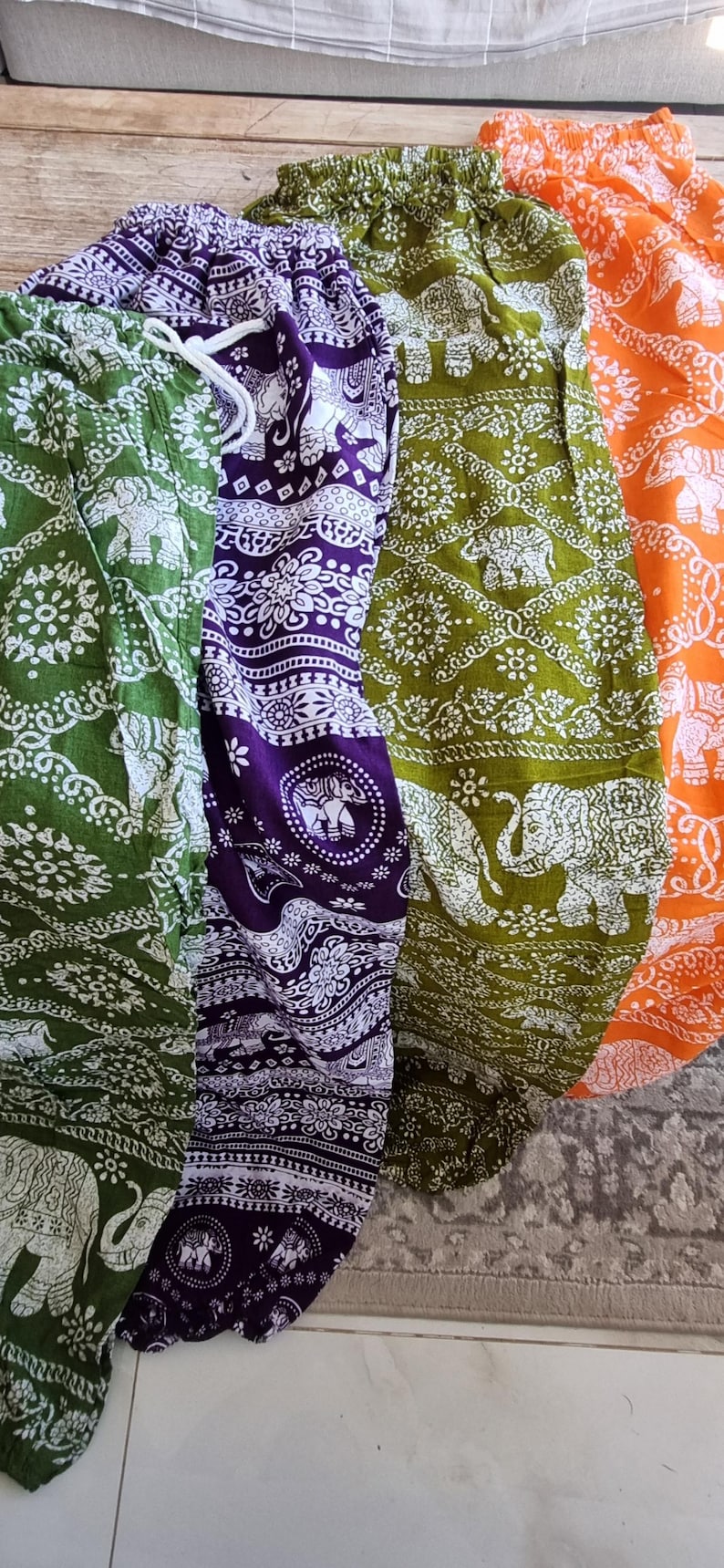 May include: Three pairs of elephant print pants in green, purple, and orange. The pants have a white elephant design on a dark background.