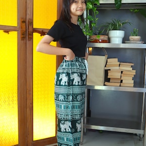 May include: A woman wearing a black t-shirt and green pants with a white elephant print. The pants have an elastic waistband and a drawstring.