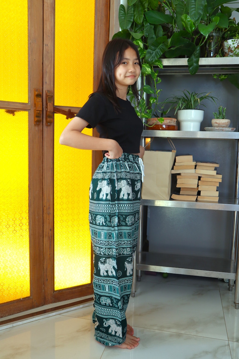 May include: A woman wearing a black t-shirt and green pants with a white elephant print. The pants have an elastic waistband and a drawstring.