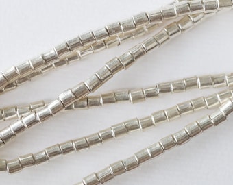 May include: A strand of silver beads, each bead is a small cylinder with a textured surface.