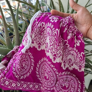 May include: Pink and white patterned fabric with a white drawstring. The fabric has a paisley design with white elephants.