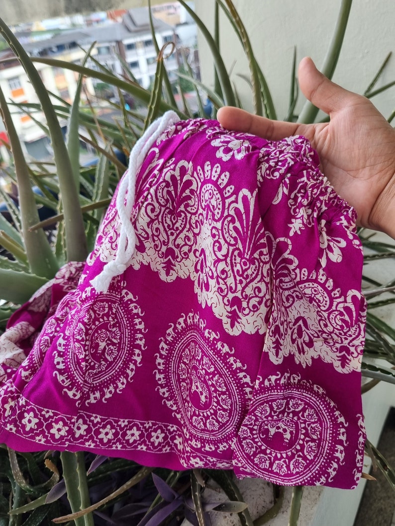 May include: Pink and white patterned fabric with a white drawstring. The fabric has a paisley design with white elephants.