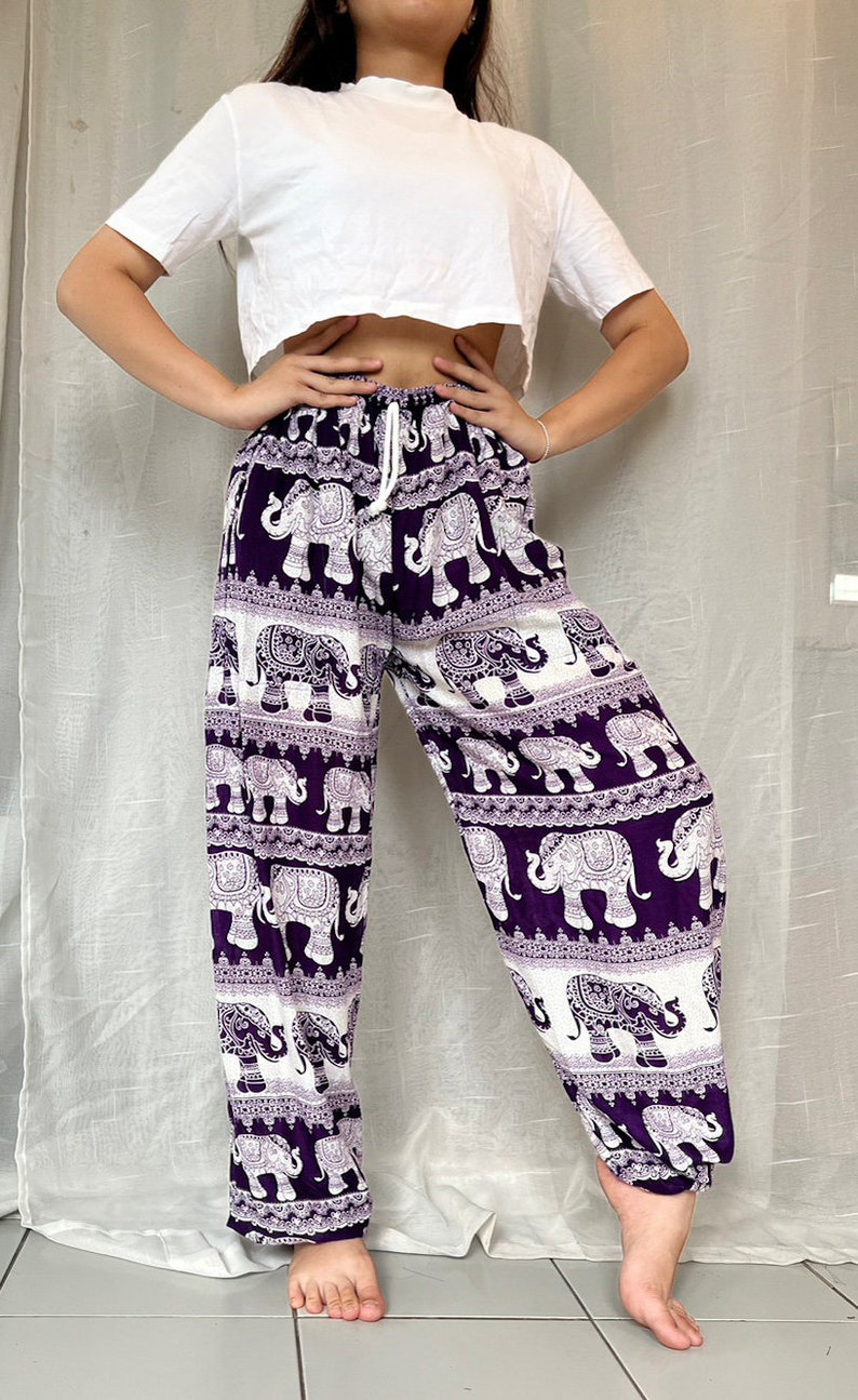 May include: Purple pants with a white elephant print. The pants have an elastic waistband and a drawstring.