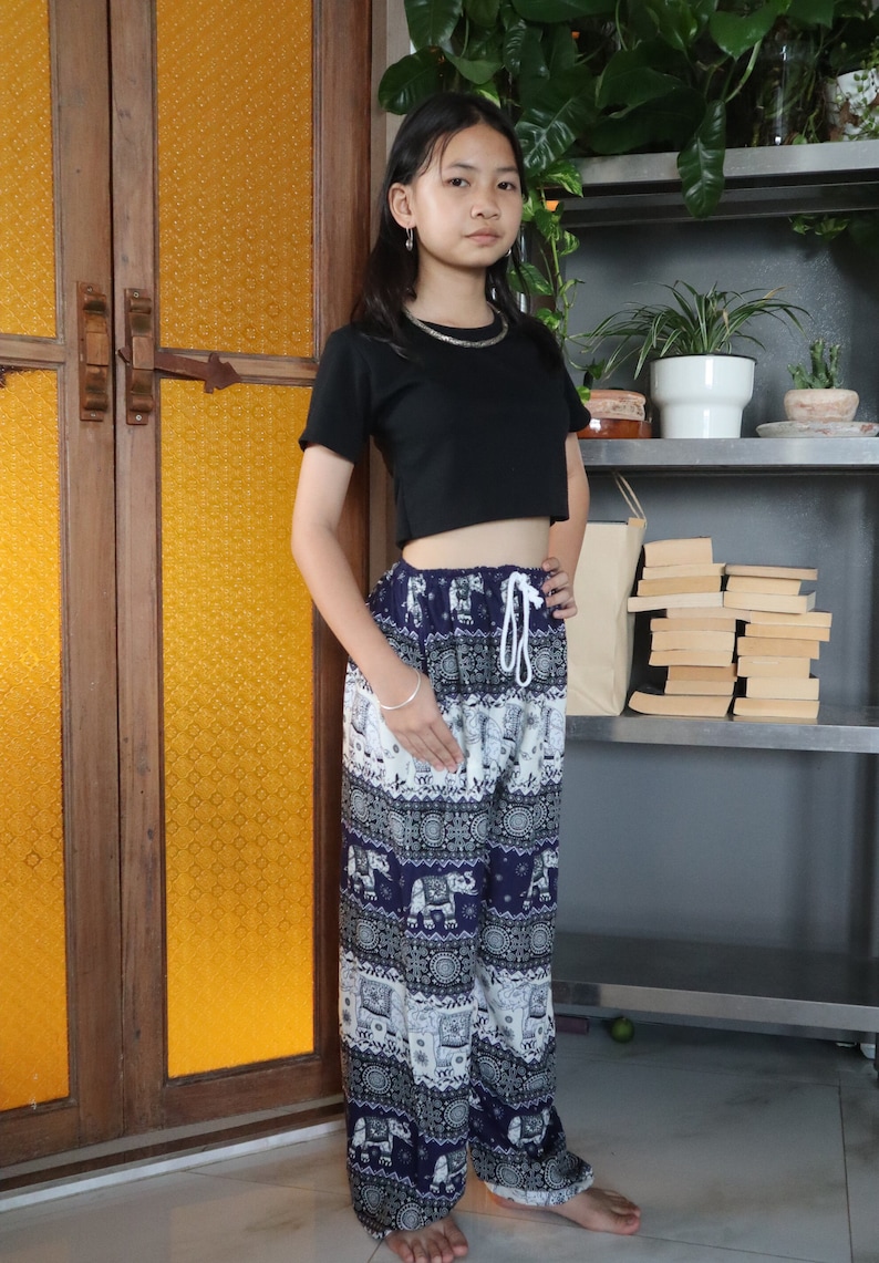 May include: A person wearing a black cropped top and blue and white patterned pants with an elephant design. The pants have a drawstring waist.