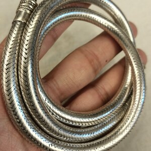 Pu&ograve; includere: Una collana a catena di serpente d'argento con finitura testurizzata. La catena &egrave; avvolta e sembra essere composta da piccoli anelli intrecciati.