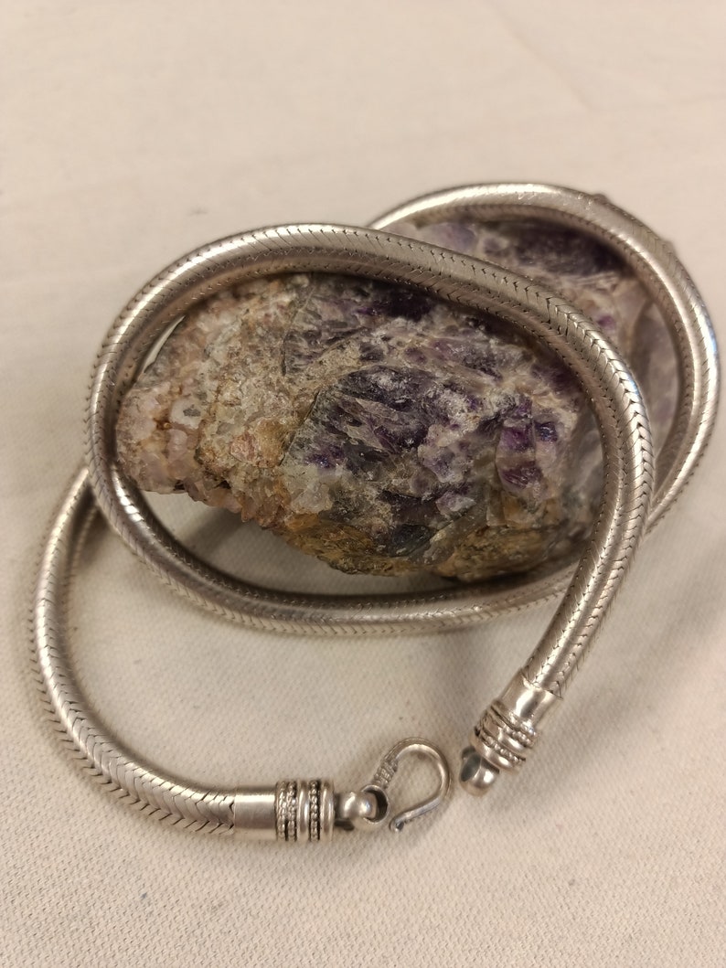 Pu&ograve; includere: Una collana a catena di serpente d'argento con una chiusura. La catena &egrave; avvolta attorno a una pietra viola e grigia.
