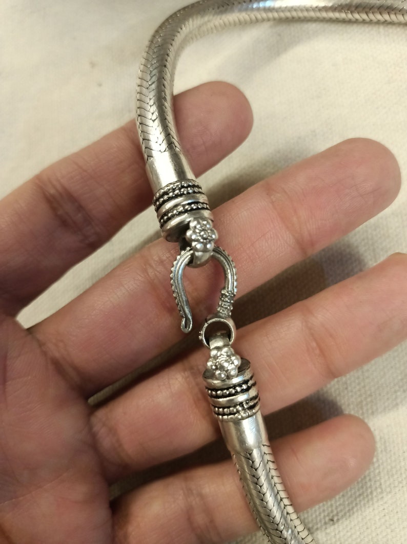 Pu&ograve; includere: Collana a catena di serpente in argento con una chiusura decorativa. La catena &egrave; realizzata con piccoli anelli intrecciati che ricordano le squame di un serpente.
