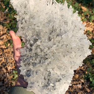 Może przedstawiać: Duży skupisko przezroczystych kryształ&oacute;w kwarcu z srebrzystoszarą macierzą mineralną. Kryształy są spiczaste i mają szorstką fakturę.