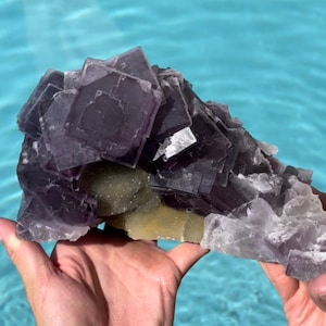 May include: A large purple fluorite crystal cluster with a smaller green crystal cluster at the base. The crystal is a natural formation with many facets and a rough texture.