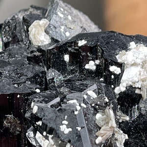 Pu&ograve; includere: Un gruppo di cristalli di turmalina nera con un bagliore argenteo. I cristalli sono raggruppati in una formazione naturale grezza.