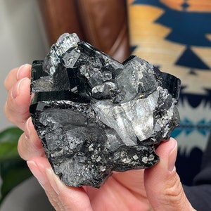 Pu&ograve; includere: Un grande ammasso di cristalli nero e argento con una texture ruvida e naturale. Il cristallo ha una forma angolare e appuntita ed &egrave; composto da pi&ugrave; sfaccettature.