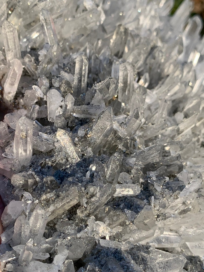 Może przedstawiać: Gromada przezroczystych kryształ&oacute;w kwarcu z szarą, metaliczną podstawą. Kryształy są ostre i spiczaste, a ich układ jest przypadkowy.