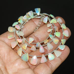 Può includere: Una collana con pietre preziose di opale iridescente. Gli opali sono tagliati in forme irregolari e infilati su una catena d'argento. Le pietre preziose mostrano una gamma di colori, tra cui bianco, rosa, giallo e verde.