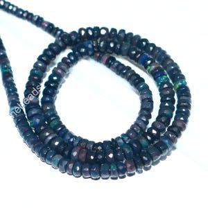 May include: A strand of faceted, dark blue opal beads. The beads have a polished, reflective surface and are strung together to form a necklace. The beads have flashes of green, blue, and red. The beads are approximately 4mm in diameter.