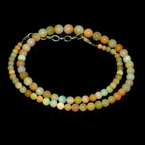 May include: A necklace made of round, multicolored opal beads. The beads range in color from pale yellow and green to orange and pink. The necklace is secured with a silver clasp and chain.