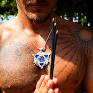 May include: A silver pendant necklace with a triangular design and blue accents. The necklace is worn on a silver chain. The person wearing the necklace has tattoos on their chest and shoulders.