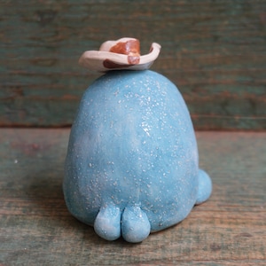May include: A blue ceramic figurine wearing a white and brown cowboy hat. The figurine has a textured surface and three small feet.