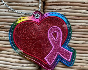 May include: A rainbow heart-shaped charm with a pink ribbon inside. The charm is attached to a silver chain.