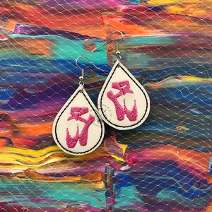 Könnte beinhalten: Ein Paar tropfenförmige Ohrringe mit weißem Hintergrund und rosa gestickten Designs. Die Ohrringe hängen an silbernen Haken.