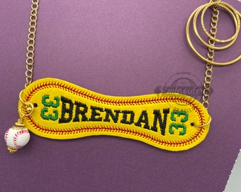 May include: A gold chain necklace with a yellow leather baseball-shaped pendant that says "BRENDAN 33" in black and green embroidery. A small white baseball charm hangs from the pendant.
