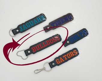 May include: Five black leather keychains with different colored embroidered team names: Jaguars, Tigers, Bulldogs, Colts, and Gators.
