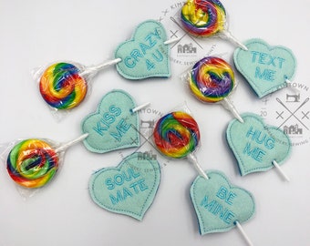 May include: Six heart-shaped felt ornaments with embroidered messages: "Crazy 4 U", "Kiss Me", "Soul Mate", "Text Me", "Hug Me", and "Be Mine". Each ornament is attached to a lollipop with a rainbow swirl design.