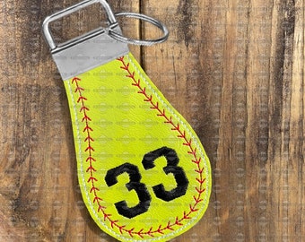 May include: A yellow softball keychain with red stitching and the number 33 in black. The keychain has a silver metal ring.