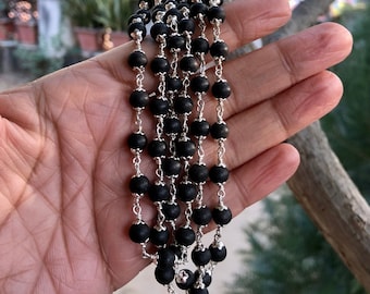 May include: A black beaded necklace with silver chain links. The necklace is made of multiple strands of beads and is hanging from a hand.