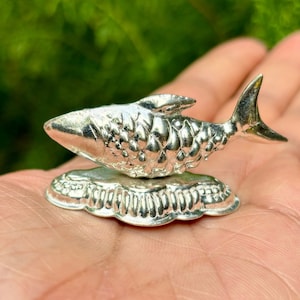 May include: A silver fish figurine with a detailed, scaly design, perched on a decorative base. The figurine is a traditional symbol of good luck and prosperity.
