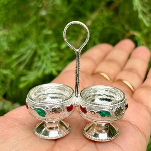 Può includere: Un doppio saliera in argento con manico. Le saliere sono decorate con accenti in smalto verde e rosso.