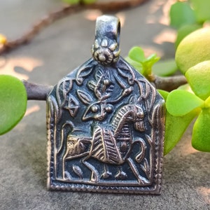 May include: A silver pendant with a detailed design of a horse and a tree. The pendant is in a square shape with a decorative border.