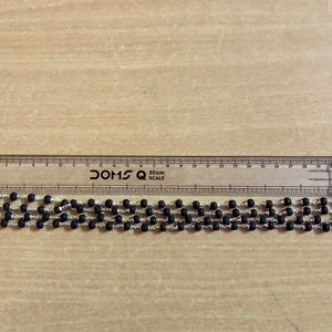 May include: A black beaded necklace with silver accents, measured against a ruler. The necklace is approximately 30 cm long.