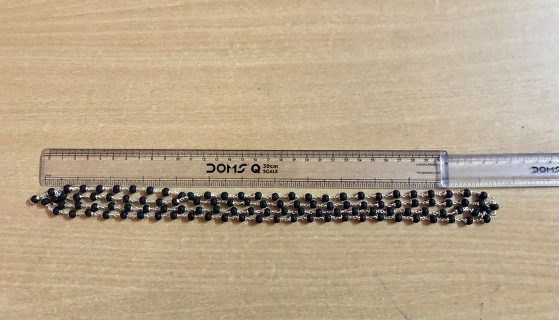 May include: A black beaded necklace with silver accents, measured against a ruler. The necklace is approximately 30 cm long.