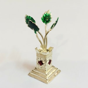 May include: A silver decorative plant with green leaves and a red base. The plant is in a silver vase with intricate designs.